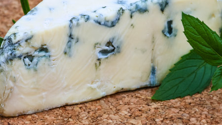 A detailed view of creamy blue cheese with distinct blue veins, accented by vibrant green mint leaves on a textured surface.の写真素材