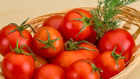 A close-up view of plump, vibrant red tomatoes with green stems, artfully arranged in a rustic woven basket, ready for use.の写真素材