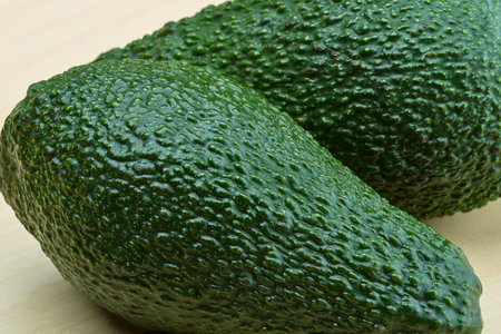 Close-up of two bumpy, dark green Hass avocados, showcasing their unique textured skin against a neutral background.の写真素材