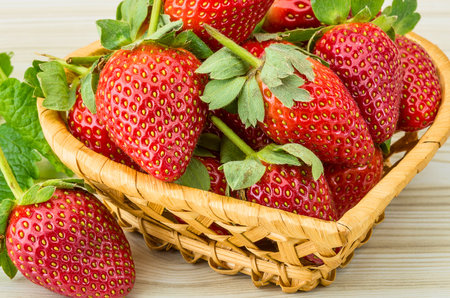 A close-up shot of ripe, red strawberries overflowing from a rustic woven basket, garnished with fresh green leaves.の写真素材