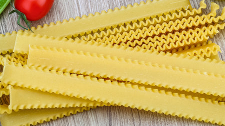 A pile of uncooked lasagna noodles with distinctive ruffled edges, showcasing their texture and color on a rustic wooden background.の写真素材