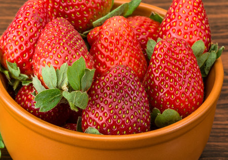 A vibrant close-up showcases a generous portion of plump, red strawberries with green stems nestled in a warm-toned ceramic bowl.の写真素材