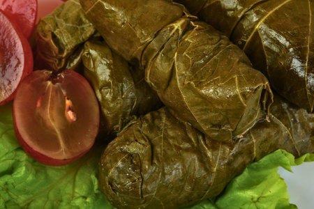 A close-up view of savory stuffed grape leaves, garnished with vibrant tomato slices and crisp lettuce, ready to be enjoyed.の写真素材