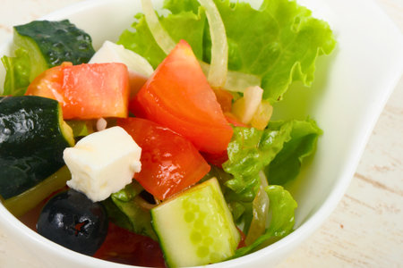 A vibrant close-up of a refreshing salad featuring crisp lettuce, juicy tomatoes, cool cucumbers, and creamy feta cheese in a white bowl.の写真素材