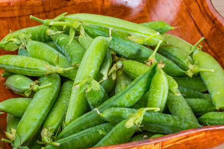 A close-up shot of numerous bright green pea pods, freshly picked and piled high in a rustic wooden bowl.の写真素材