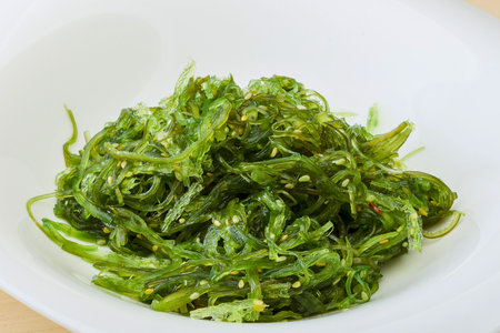 A close-up of a vibrant green seaweed salad, likely wakame, seasoned with sesame seeds and served in a simple white dish.の写真素材