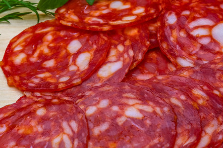 Thinly sliced spicy Italian salami with visible white fat marbling, creating a rich red and white pattern.の写真素材