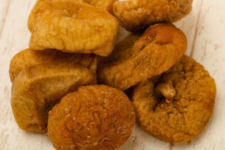 A pile of golden brown dried figs is shown from a top down perspective on a textured wooden background.の写真素材