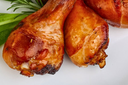 Close-up of two golden-brown roasted chicken drumsticks, glistening with juices, garnished with fresh rosemary and green leaves.の写真素材