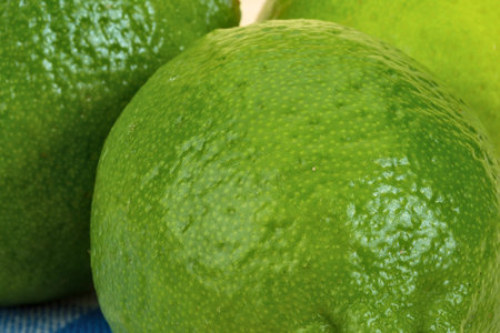 A detailed macro shot showcasing the bumpy, textured skin of several bright green limes,...