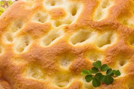 Close-up view of a rustic focaccia bread, showcasing its golden crust, dimpled surface, and a sprig of fresh green herb.の写真素材