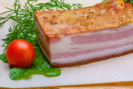 A close-up of a thick slice of smoked pork belly, garnished with fresh dill and a cherry tomato.の写真素材