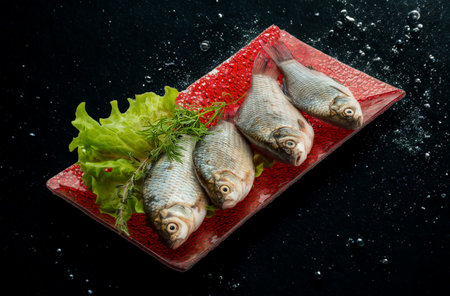 Four whole, uncooked fish are arranged on a vibrant red platter with a side of fresh green lettuce...