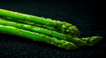 A close-up shot of vibrant green asparagus spears with water droplets, set against a dark, textured background.の写真素材