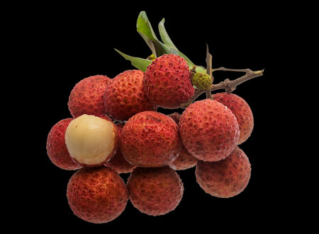 A vibrant bunch of fresh lychee fruits, mostly red with one pale fruit, clustered on a dark background.の写真素材