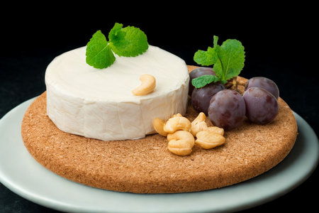 A round of soft white cheese sits atop a cracker, garnished with fresh mint, grapes, and nuts.の写真素材