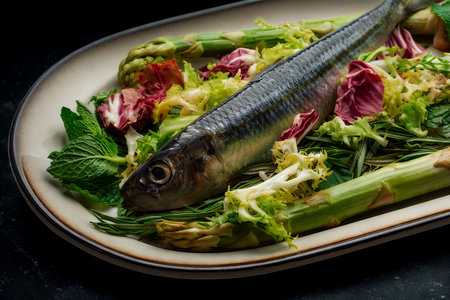 A whole cooked fish rests atop a vibrant salad of mixed greens and tender asparagus spears on an oval plate.の写真素材