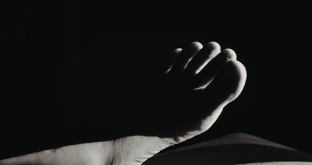 A close-up black and white image of a hand against a dark background, emphasizing the mood and...
