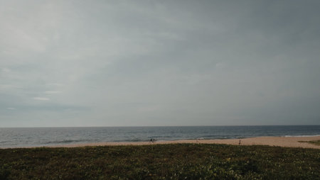 A serene beach scene featuring a cloudy sky, calm ocean waters, and a small stretch of sandy shore.