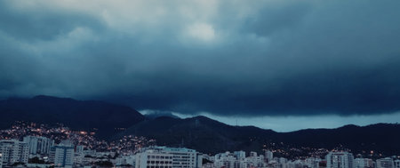 A panoramic view of a city nestled between mountains, with tall buildings and a cloudy sky overhead.