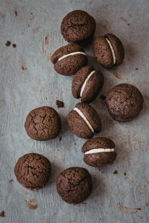 A close-up image of several chocolate cookies, some filled with cream, arranged on a textured...