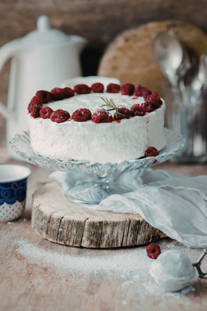 A beautifully decorated raspberry cake with white frosting and fresh raspberries on top, placed on a...