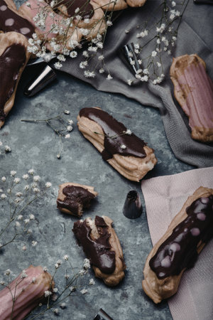 A collection of beautifully arranged chocolate eclairs on a rustic table, adorned with delicate flowers and baking tools.の写真素材