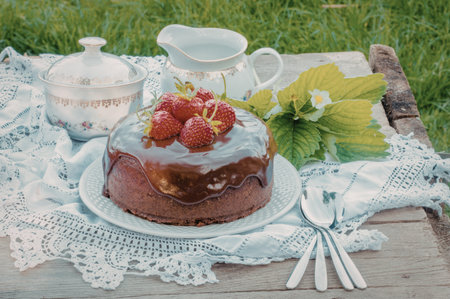 A beautifully decorated cake with fresh strawberries sits on a rustic wooden table, accompanied by vintage tableware and a bouquet of greenery.の写真素材