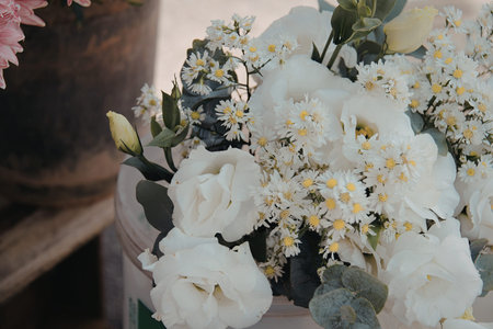 A close-up view of a beautiful bouquet of white roses and small white flowers arranged in a vase. The flowers are complemented by green leaves, creating a serene and sophisticated atmosphere.の写真素材