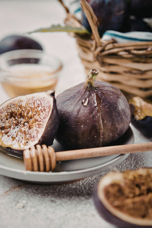 A close-up image of fresh figs, some sliced open and drizzled with honey, accompanied by a jar of honey and a wooden honey dipper, with flatbreads in the background.の写真素材