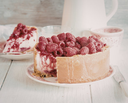 A delicious slice of cheesecake topped with fresh raspberries, served on a white plate with a creamy...