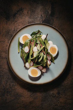 A vibrant spinach salad topped with boiled eggs, radishes, and green onions, served on a blue plate.の写真素材