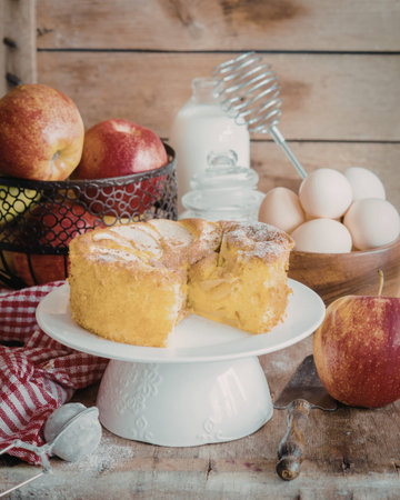 A close-up of a freshly baked apple cake displayed on a white cake stand, surrounded by fresh...