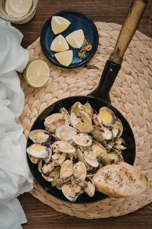 A skillet filled with steaming clams, garnished with lemon slices and herbs, accompanied by a piece of toasted bread and a lemon wedge on the side.の写真素材