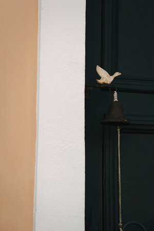 A close-up image of a bird sculpture perched on a dark green door, with an adjacent white wall and an orange wall in the background.の写真素材
