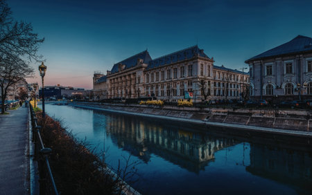 A serene image of historic buildings lining a calm river at dusk, with reflections on the water and a clear sky overhead.の写真素材