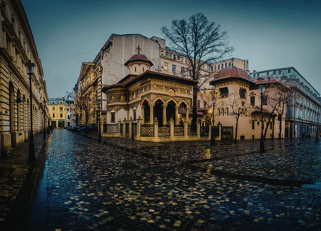 A picturesque image of a historic church situated in a rainy urban environment. The cobblestone street reflects the surrounding architecture, including the church's ornate facade and nearby buildings.の写真素材