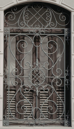 A detailed view of a wrought iron window grill featuring elaborate scrollwork and geometric...