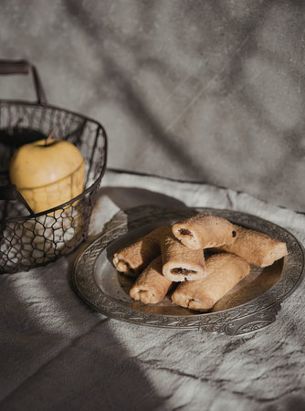 A plate of golden-brown pastry rolls is displayed on a textured tablecloth, accompanied by a basket...