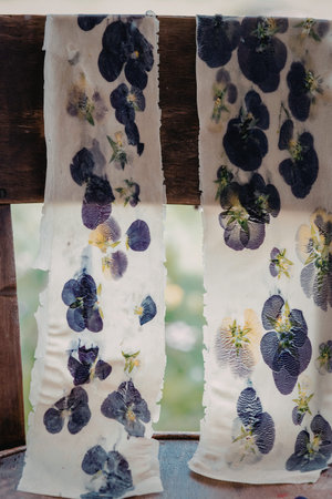 This image showcases beautiful handmade paper adorned with pressed flowers, hanging against a rustic...