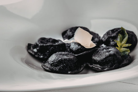 A close-up image of a white plate holding several dark dumplings, topped with a piece of cheese and...