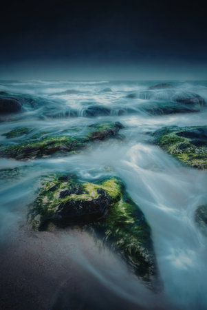 A tranquil coastal scene featuring smooth, rounded rocks covered in vibrant green moss. The water flows gently around the rocks, creating a serene and calming atmosphere.の写真素材