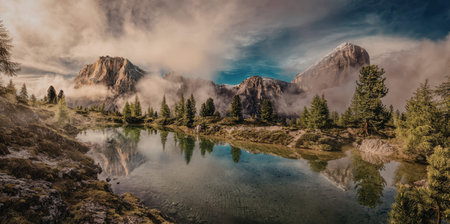 A tranquil mountain lake reflects the surrounding peaks and trees under a dramatic sky during...