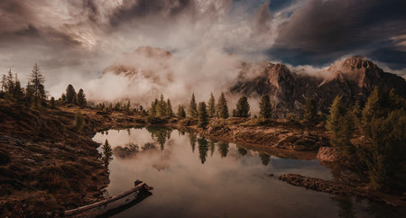 A tranquil mountain lake reflects the surrounding landscape and dramatic clouds during sunset, creating a stunning natural scene.の写真素材