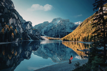 A tranquil scene of a mountain lake reflecting the surrounding peaks and autumn foliage. A solitary...