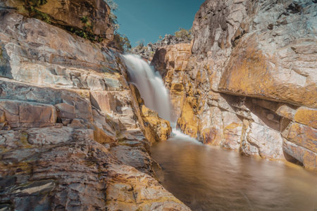 A tranquil waterfall cascades down a rugged, rocky cliff, surrounded by natural beauty.