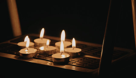 A close-up image of several lit candles arranged on a dark surface, creating a serene and intimate...