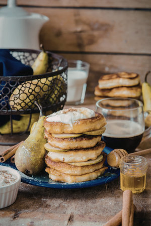A stack of golden-brown pear pancakes topped with a dollop of cream and a sprinkle of cinnamon,...