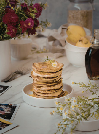 A stack of golden-brown pancakes topped with butter and a small flower, placed on a white plate....