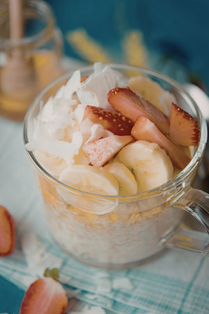 A glass mug filled with creamy oatmeal topped with sliced bananas, fresh strawberries, and coconut...